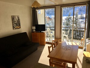 Una sala de estar con un sofá oscuro, una mesa de comedor de madera y un televisor sobre un mueble de madera. Amplias ventanas ofrecen vistas a un paisaje nevado.