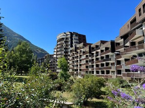 Un hotel de varios pisos con balcones, rodeado de vegetación y una montaña al fondo.