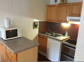 Una cocina compacta equipada con microondas, lavaplatos, fregadero y estufa.