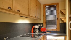 Une cuisine compacte avec des meubles en bois, un plan de travail noir, un grille-pain rouge, une machine à café et un lave-vaisselle encastré.