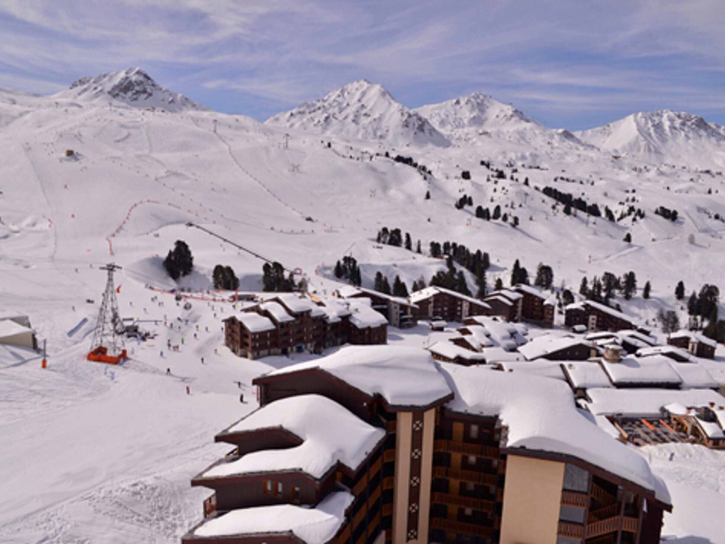 A snow-covered mountain resort with chalet-style buildings, ski slopes, and a ski lift.