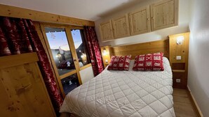 Une chambre à coucher avec un lit, une tête de lit en bois, des rideaux rouges et une fenêtre donnant sur un beau paysage.