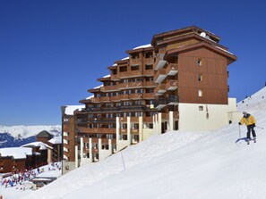 Un hôtel à plusieurs étages doté de balcons, de pistes de ski et où l’on peut apercevoir un skieur.