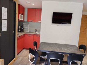 A compact kitchen with red cabinets, a black countertop, and a flat-screen TV mounted on the wall. - Renovated 2-room apartment, balcony, pets allowed, parking (La Plagne Montchavin Les Coches)