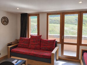 Une pièce avec un canapé, une table en bois et de grandes fenêtres donnant sur un paysage verdoyant.