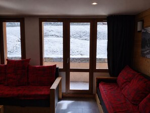 A room with a wooden floor, a red sofa, and a window with a view of a snowy landscape. - Renovated 2-room apartment, balcony, pets allowed, parking (La Plagne Montchavin Les Coches)