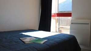 A room with a bed, a window with a view of mountains, and a radiator. - Bright apartment near ski lifts, mountain corner, pets allowed (Briançon)