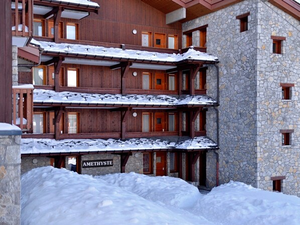 A multi-story wooden building with stone walls, snow-covered balconies, and a sign reading "AMETHYSTE".