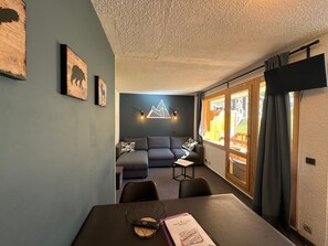 A room with a dining table, a sofa, and a view through a window.