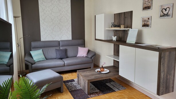 A modern living room with a grey sofa, a wooden coffee table, and a small side table. There are decorative items on the shelves, including a heart-shaped frame and a sign that says "Liebe Home". - Vacation home with garden and terrace, 15 minutes from the Moselle (Blankenrath)