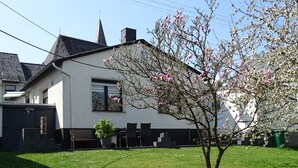 A white house with a black roof, a visible chimney, and a small garden with a tree and a potted plant. - Vacation home with garden and terrace, 15 minutes from the Moselle (Blankenrath)