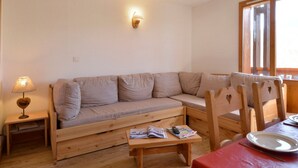 Una sala de estar acogedora con un sofá de madera, una mesita baja con revistas, una lámpara y una mesa de comedor con un plato y cubiertos.