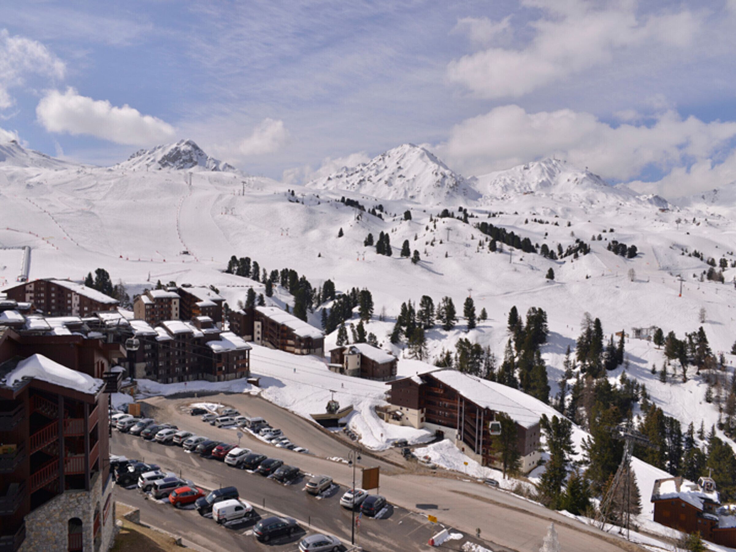 A snow-covered mountain town with a ski resort, including a parking lot and buildings with snow-covered roofs.