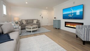 En stue med sofa, sofabord, pejs og stort tv ophængt på væggen.