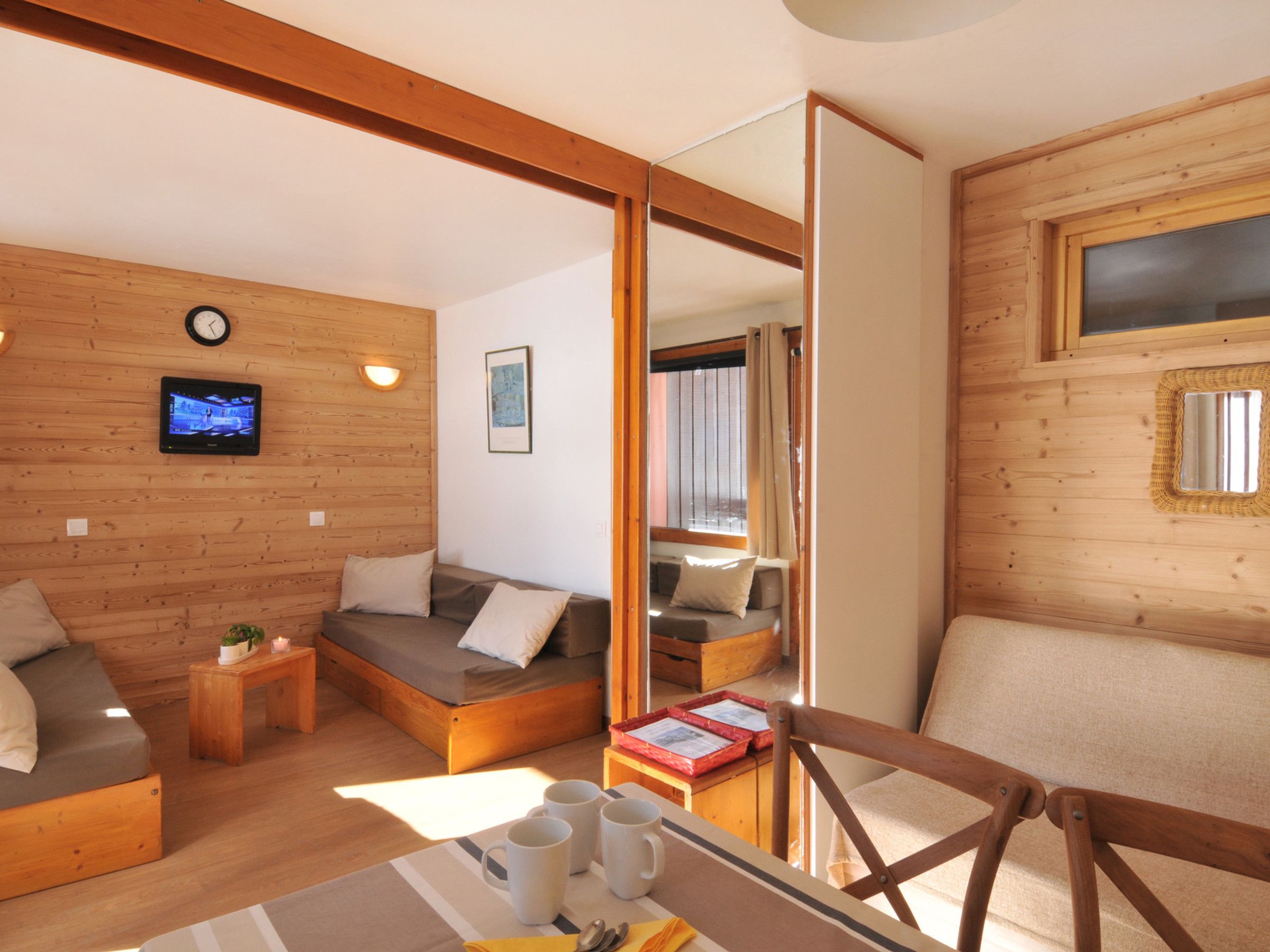 A cozy room with a bed, a sofa, a small table with mugs, and a television on the wall.