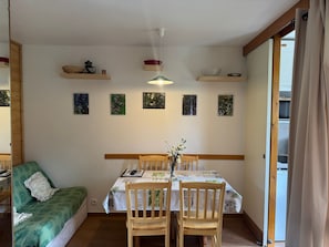 A dining area with a table set for two, flanked by wooden chairs, a green sofa, and a wooden bench. - Renovated ski-in/ski-out studio with balcony for 4 people (Belle Plagne)