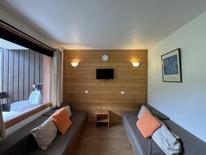 Ein Zimmer mit zwei Sofas, einem an der Wand befestigten Fernseher und einem kleinen Tisch.