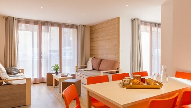 Un salon moderne avec un canapé, une table à manger avec des chaises orange et un plateau de petit-déjeuner.