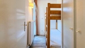 Un pasillo estrecho con una litera de madera a la derecha, un radiador a la izquierda y una puerta al final.