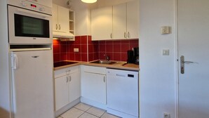 Cocina compacta con gabinetes blancos, microondas, lavavajillas y un salpicadero de azulejos rojos.