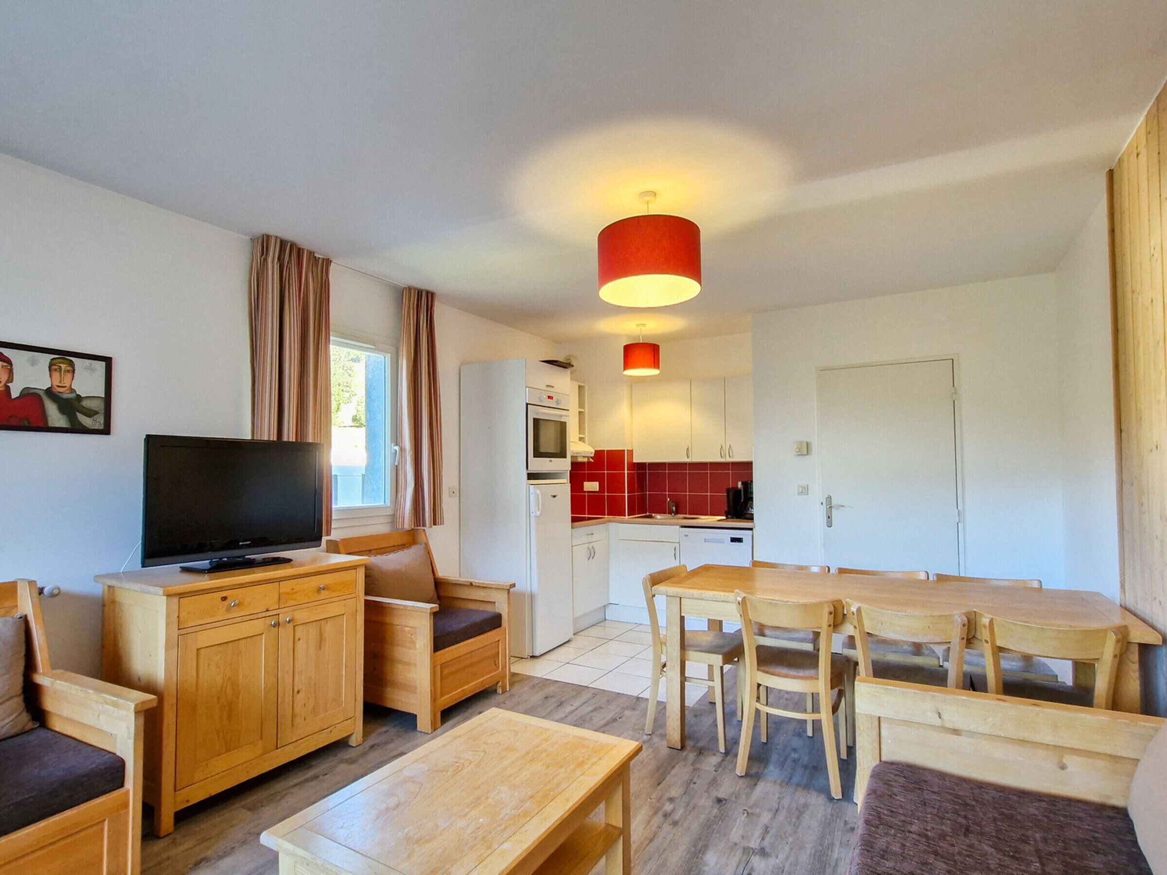 A compact living space with a TV, wooden furniture, a kitchen area, and a dining table.