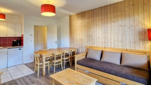 Un espacio habitable pequeño con pared de madera, un sofá, una mesa de comedor con sillas, y una zona de cocina con armarios y una cafetera.