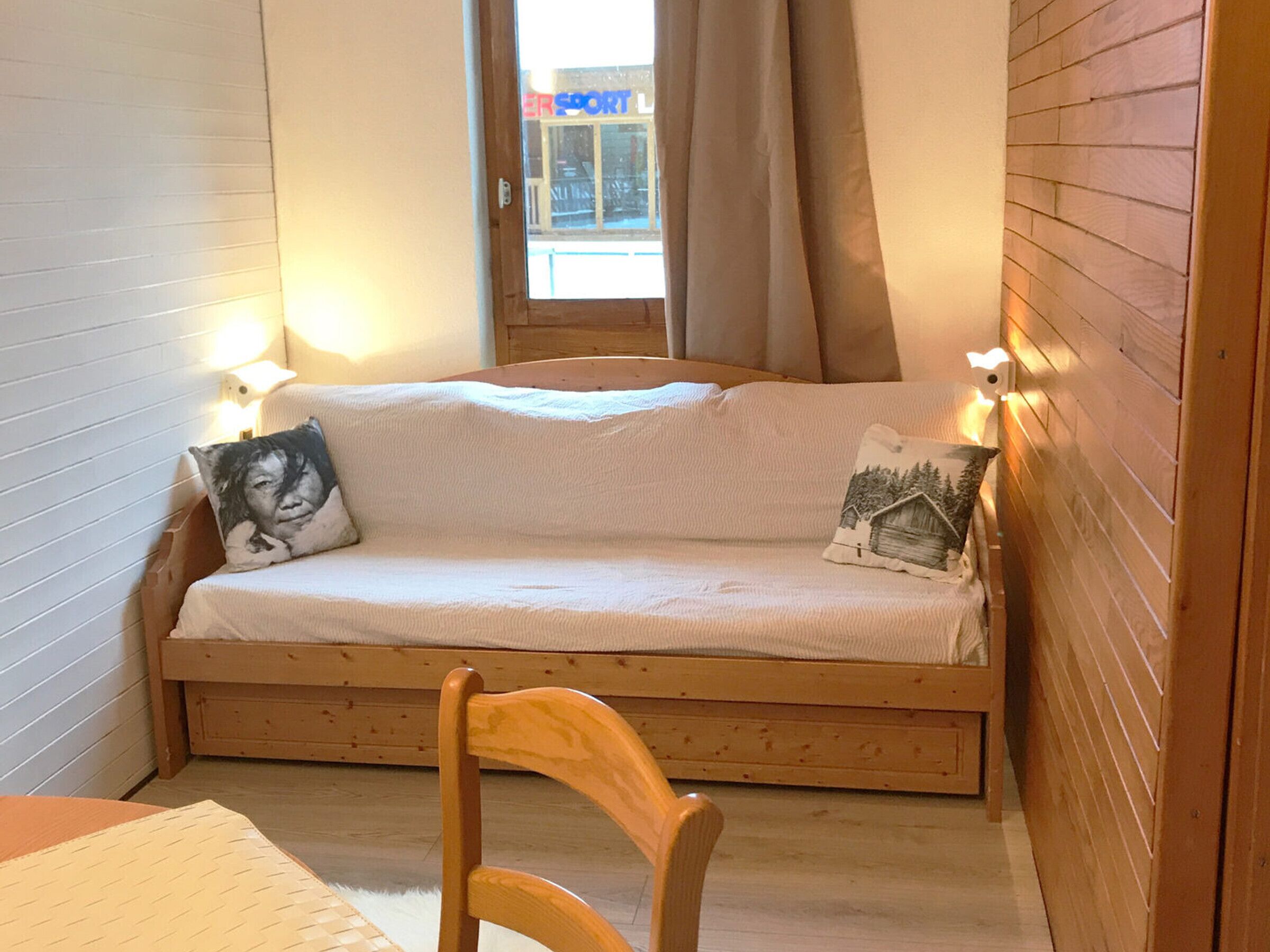 Ein kleiner, gemütlicher Raum mit einer hölzernen Bank, einem weißen Sofa mit zwei Kissen und einem Fenster mit Vorhängen.