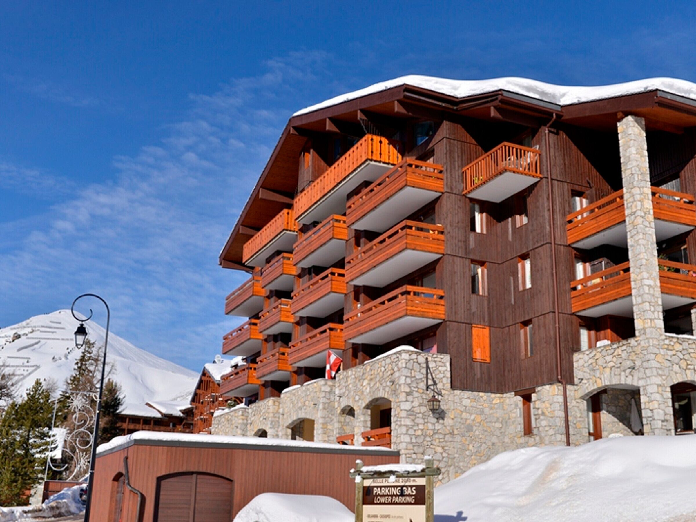A multi-story hotel with wooden balconies and stone walls, featuring a sign for parking and lower parking.