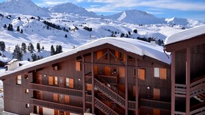 Eine Holzchalet mit mehreren Balkonen und einer Treppe, umgeben von schneebedeckten Bergen.