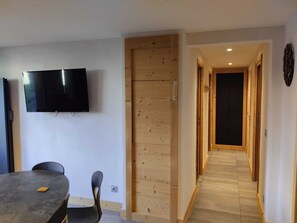 A modern interior with a flat-screen TV mounted on the wall, a dining table with chairs, and a wooden door.