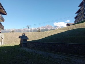 A stone wall with a small building, a grassy slope, and a mountain range in the background.