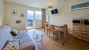 Ein gemütliches Wohnzimmer mit einer Couch, einem kleinen Tisch, einem Esstisch mit Stühlen, einem Flachbildfernseher und einer Küchenzeile mit einer Mikrowelle.