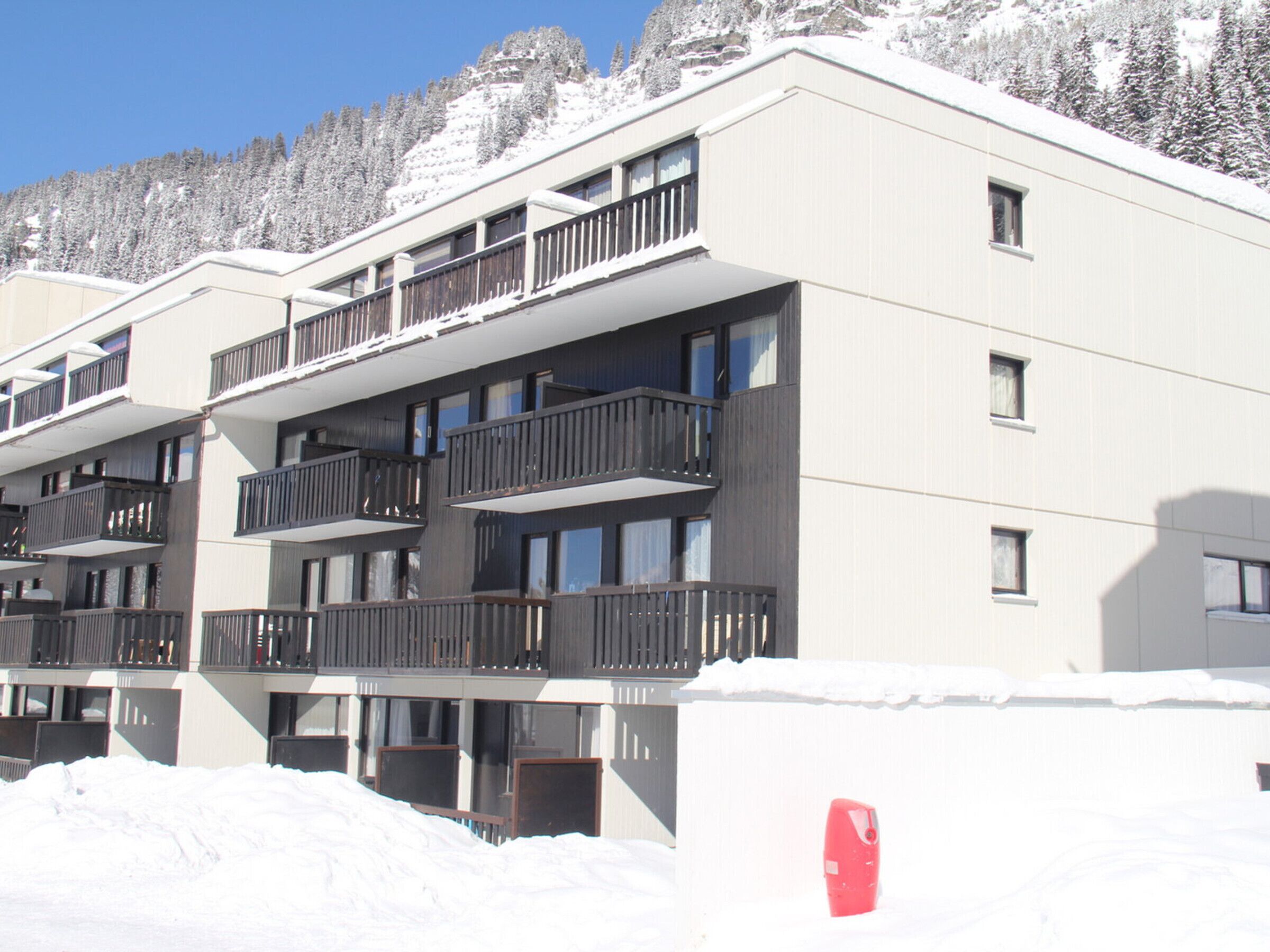 A multi-story hotel with balconies and a snowy mountain backdrop.