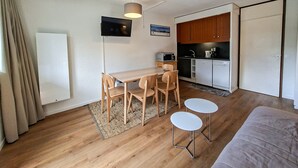 Ein gemütlicher Raum mit Holztisch, vier Stühlen, einer kleinen Küche mit Mikrowelle, Spüle und Geschirrspüler sowie einem Einzelbett.