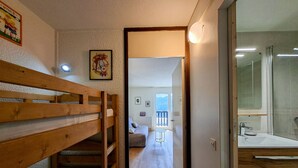 Ein schmaler Flur führt zu einem Schlafzimmer mit Etagenbett, einem Badezimmer mit Glasdusche und einem Balkon mit Blick.