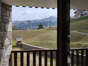 Varanda com parede de pedra e vista para paisagem acidentada, com edifícios e montanhas ao longe.