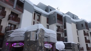 Un hôtel à plusieurs étages, doté de balcons enneigés, de piliers en pierre et d’enseignes de café au néon.