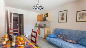 A compact living space with a dining table set for breakfast, a sofa, a kitchenette, and a door leading to another room. - Cozy studio with ski shuttle and private locker - 4 guests (La Salle-les-Alpes)