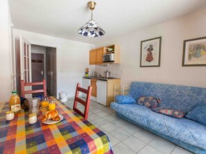A compact living space with a dining table set for breakfast, a sofa, a kitchenette, and a door leading to another room.