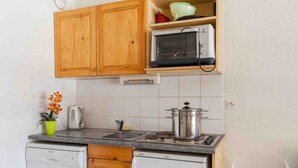 A compact kitchen with wooden cabinets, a built-in microwave, a sink, and a dishwasher. - Cozy studio with ski shuttle and private locker - 4 guests (La Salle-les-Alpes)