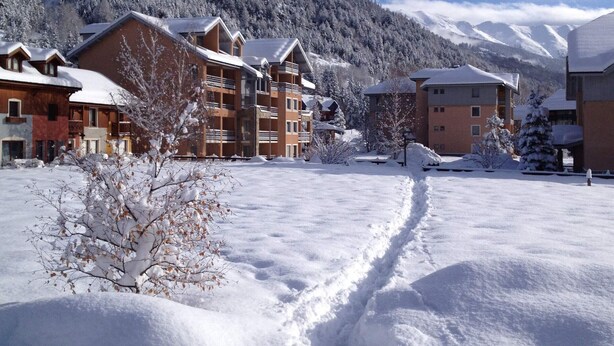 A snow-covered resort with multiple chalet-style buildings, a ski slope, and a mountainous backdrop. - Cozy studio with ski shuttle and private locker - 4 guests (La Salle-les-Alpes)