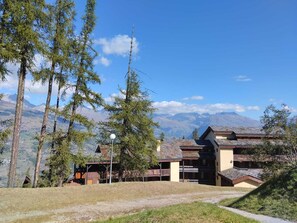 A mountain lodge with a view of distant mountains, surrounded by tall trees. - Renovated Apartment 5 ppl - Pets Allowed, Free Parking (La Plagne Montchavin Les Coches)