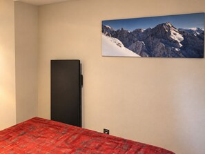 Ett sovrum med en säng, en svart garderob och en tavla med ett bergsmotiv på väggen.