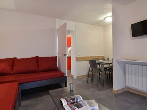 Un espacio habitable pequeño con un sofá rojo, una mesa de comedor con sillas y un televisor montado en la pared.