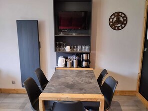 A dining area with a long table, black chairs, a television on a shelf, and a clock on the wall.