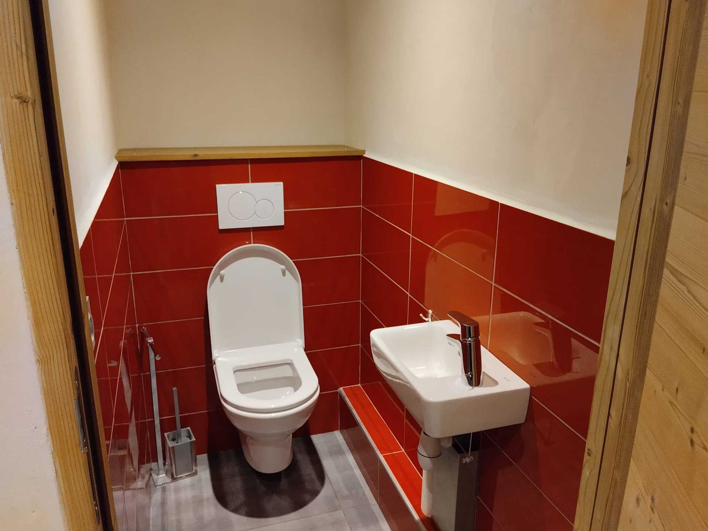 Ett litet badrum med en vit toalett, ett handfat och väggar klädda med röda kakelplattor.