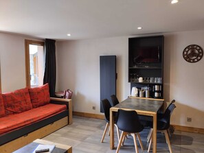 Un salon moderne comprenant un canapé, une table à manger avec des chaises, un téléviseur et un coin cuisine avec des étagères.