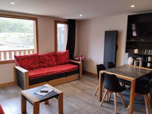 A cozy room with a sofa, a dining table, chairs, a TV, and a window with a view.
