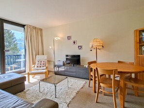 A living room with a sofa, a glass coffee table, a dining table with chairs, a TV, and a lamp.