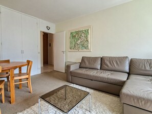 Un salon avec un canapé en cuir marron, une table basse en verre, une table à manger en bois avec des chaises et un meuble blanc.